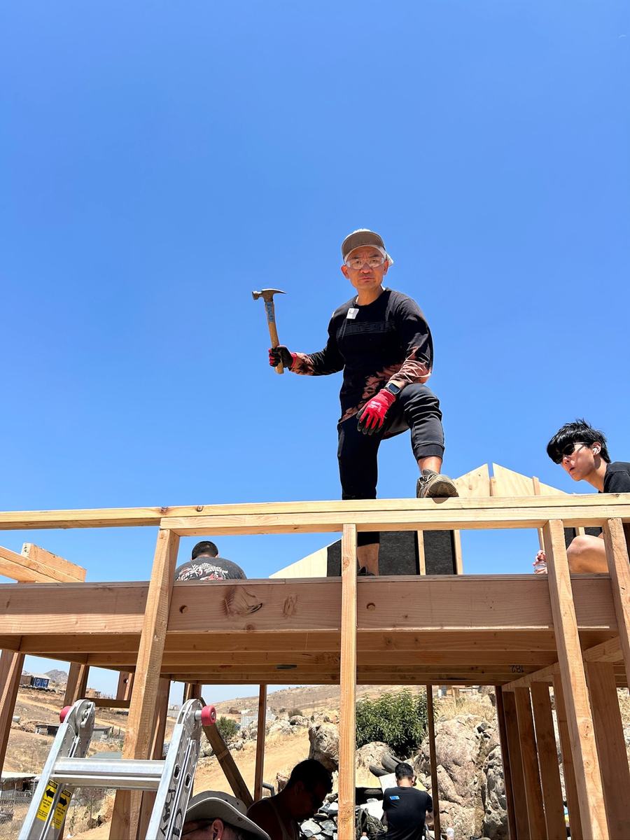 A young volunteer hammering on a roof beam against the sky